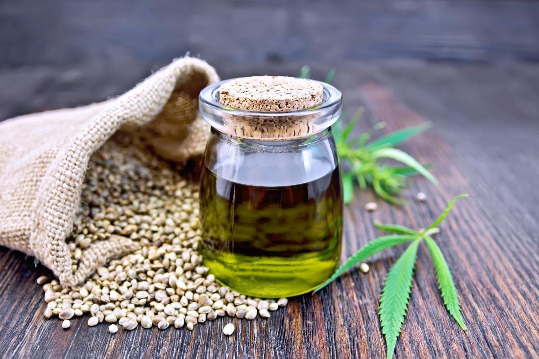 Hemp seeds in a sack and hemp leaves are positioned beside a jar of hempseed oil